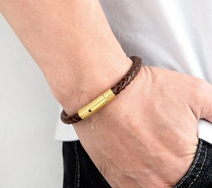 Detail van donkerbruine gevlochten leren armband met een getextureerde gouden metalen sluiting