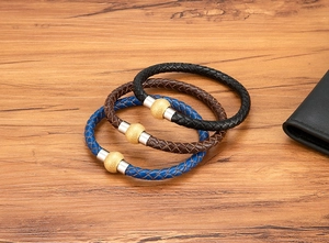 Dettaglio macro di bracciali in pelle intrecciata nero, marrone e blu con chiusura in acciaio