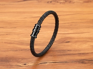Close-up of black braided leather bracelet with magnetic metal clasp on wooden surface