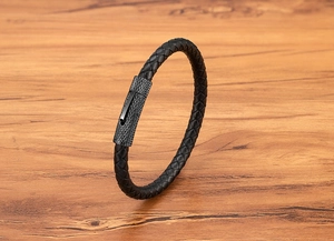 Detail van zwarte gevlochten leren armband met getextureerde metalen magneetsluiting