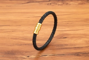 Detail of black braided leather bracelet with matte gold magnetic clasp on wood