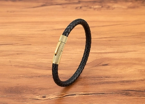 Detail van een zwart gevlochten leren armband met een gouden getextureerde magneetsluiting