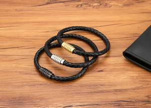 Close-up of woven leather bracelets with magnetic clasps in gold silver and black on wood