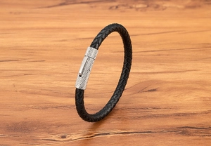 Detailopname van zwarte gevlochten leren armband met zilveren metalen sluiting op hout