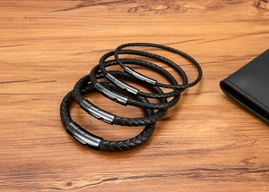 Detail view of woven black leather bracelets with black metal magnetic clasps on wood