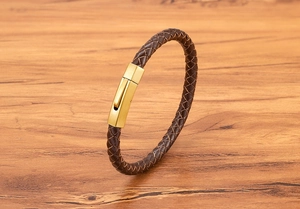 Detail view of brown braided leather bracelet with a matte gold magnetic buckle on wood