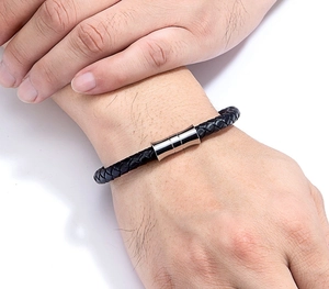 Close-up of black braided leather bracelet with silver magnetic cylindrical clasp on wrist