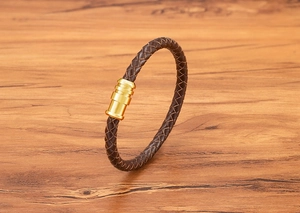 Detail of a brown braided leather bracelet with a polished gold magnetic metal clasp