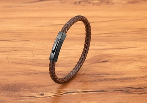 Detail of brown braided leather bracelet with black brushed metal magnetic clasp on wood