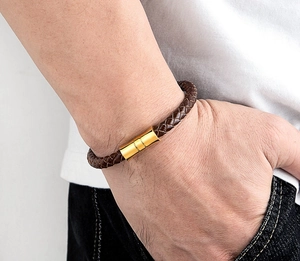 Close-up of a brown braided leather bracelet with a gold magnetic clasp on a man's wrist