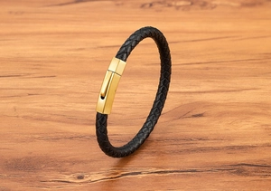 Close-up of black braided leather bracelet with golden brushed hexagonal clasp on wood