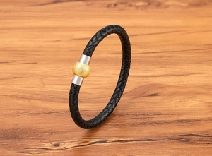 Dettaglio di un bracciale in pelle nera intrecciata con perla dorata su base in legno