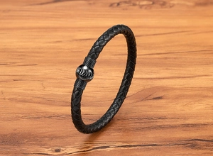 Dettaglio di bracciale in pelle intrecciata nera con chiusura magnetica in metallo zigrinato