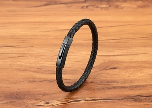 Close-up of black braided leather bracelet with matte black hexagonal metal clasp on wood