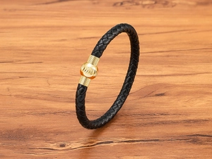 Dettaglio di bracciale in pelle intrecciata nera con perla dorata e chiusura magnetica