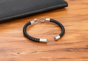Detail of infinity leather bracelet with silver magnetic clasp on a wood texture background