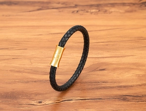 Close-up of black braided leather bracelet with a gold magnetic clasp on wood
