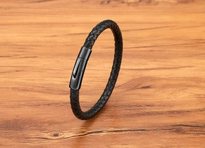 Close-up of black braided leather bracelet with matte black magnetic metal clasp on wood