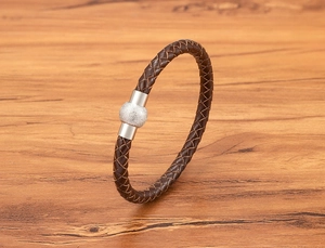 Dettaglio macro del bracciale in pelle intrecciata marrone con perla in metallo