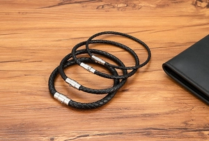 Detail of four black braided leather bracelets with silver magnetic clasps on wood