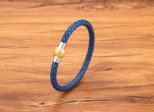 Dettaglio di bracciale in pelle intrecciata blu con chiusura magnetica argento e oro