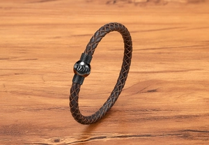 Dettaglio di bracciale in pelle intrecciata con chiusura magnetica su sfondo di legno