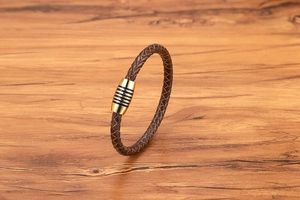 Dettaglio di un bracciale in pelle intrecciata marrone con chiusura magnetica dorata