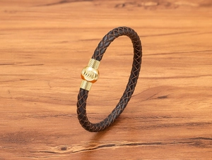 Dettaglio del bracciale in pelle intrecciata con chiusura in metallo dorato su legno