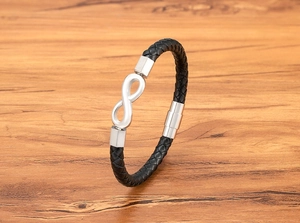 Close-up of black braided leather bracelet with silver infinity symbol on wood