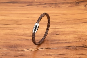 Dettaglio di un bracciale in pelle intrecciata marrone con chiusura magnetica argento a righe nere