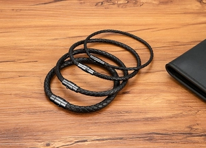 Detail of four black braided leather bracelets with matte magnetic clasps on wood