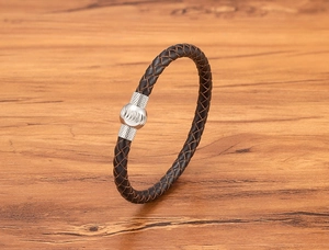 Dettaglio macro del bracciale in pelle intrecciata marrone scuro con chiusura in metallo