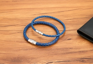 Dettaglio di bracciali in pelle blu intrecciata con fibbia magnetica su tavolo di legno