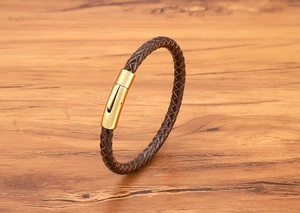 Detail eines geflochtenen braunen Lederarmbands mit poliertem Gold-Magnetverschluss