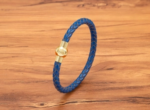 Dettaglio bracciale in pelle intrecciata blu con chiusura magnetica dorata su legno