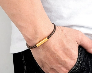 Detailed close-up of brown braided leather bracelet with rectangular gold metal buckle on wrist