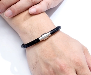 Detail of black braided leather bracelet with silver cylindrical magnetic clasp for men