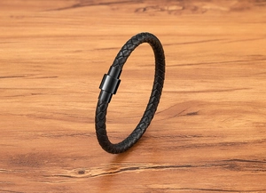 Close-up of black braided leather texture and sleek magnetic metal clasp on wooden background