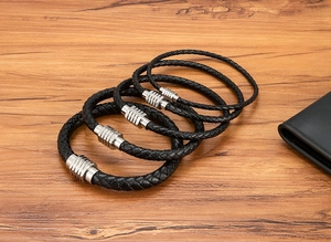 Dettaglio di quattro bracciali in pelle nera intrecciata con chiusure magnetiche