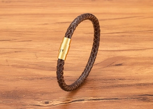 Macro del bracciale in pelle intrecciata marrone con chiusura magnetica dorata su legno