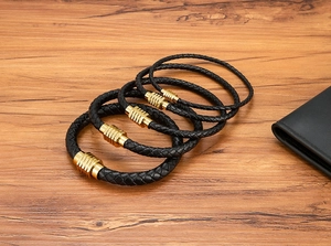 Dettaglio di cinque bracciali in pelle nera intrecciata con chiusure magnetiche dorate