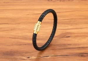 Dettaglio del bracciale in pelle intrecciata nera con chiusura magnetica dorata su legno
