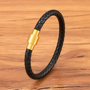 Braided black leather bracelet with golden magnetic stainless steel clasp on wood