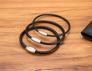 Details von drei schwarzen Lederarmbändern mit Edelstahl-Magnetverschluss auf Holzhintergrund