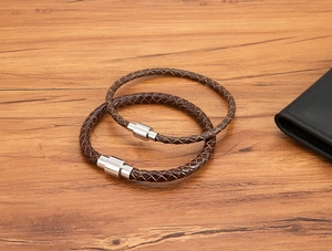 Détail de bracelets en cuir tressé marron avec fermoirs magnétiques sur bois