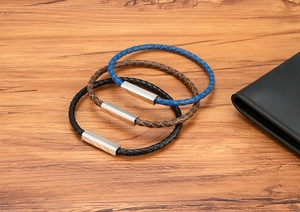 Close-up of three braided leather bracelets with silver magnetic clasps on wood table