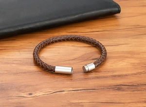 Detail of woven brown leather bracelet with silver cylindrical magnetic clasp on wood