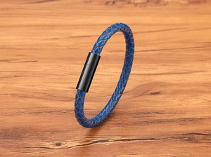 Détail d'un bracelet en cuir tressé bleu avec fermoir magnétique noir sur bois