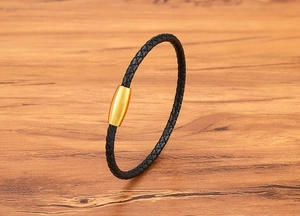 Detail eines schwarzen geflochtenen Lederarmbands mit poliertem goldenem Magnetverschluss