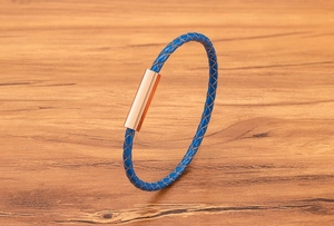Detail of blue braided leather bracelet with rose gold magnetic clasp on wooden surface
